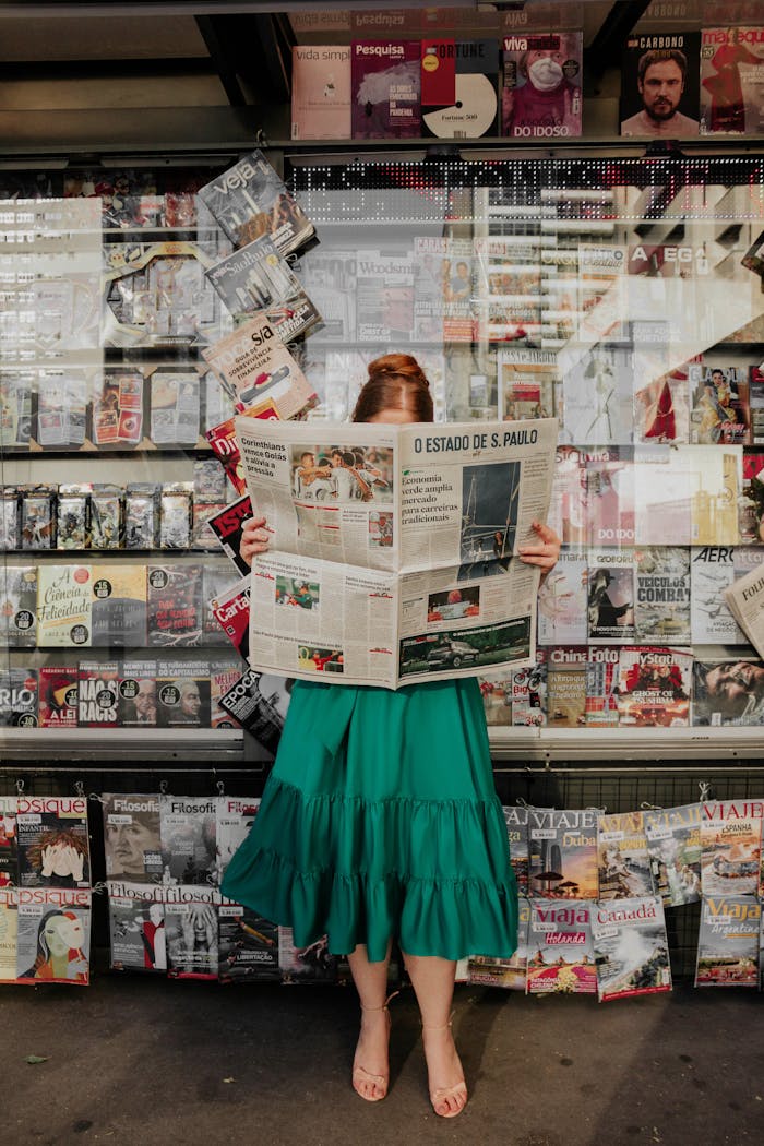 about-us Woman in green dress reading newspaper at street magazine stand outdoors.