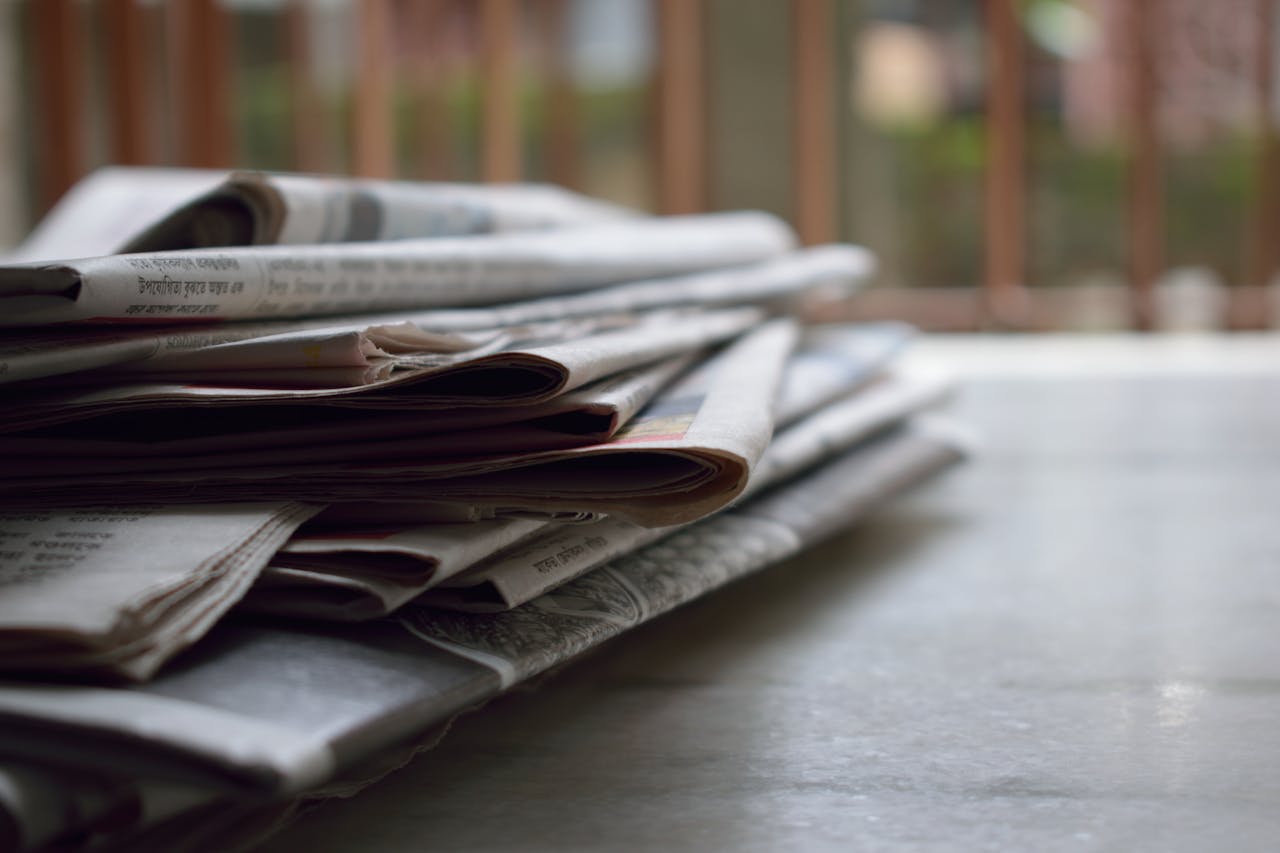 heros-img A close-up of a stack of newspapers resting on a desk, symbolizing information and media.